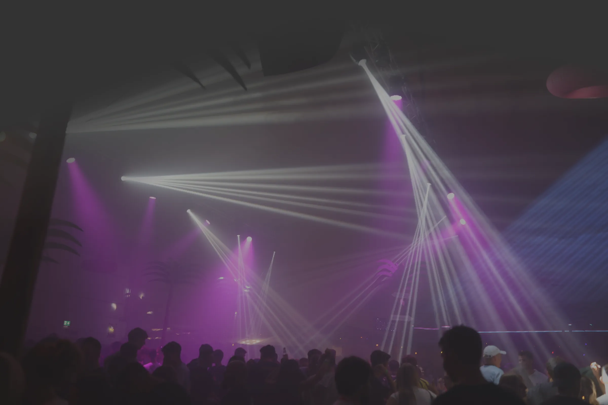 Eventhalle mit lila und weißen Lichtstrahlen über dem Publikum