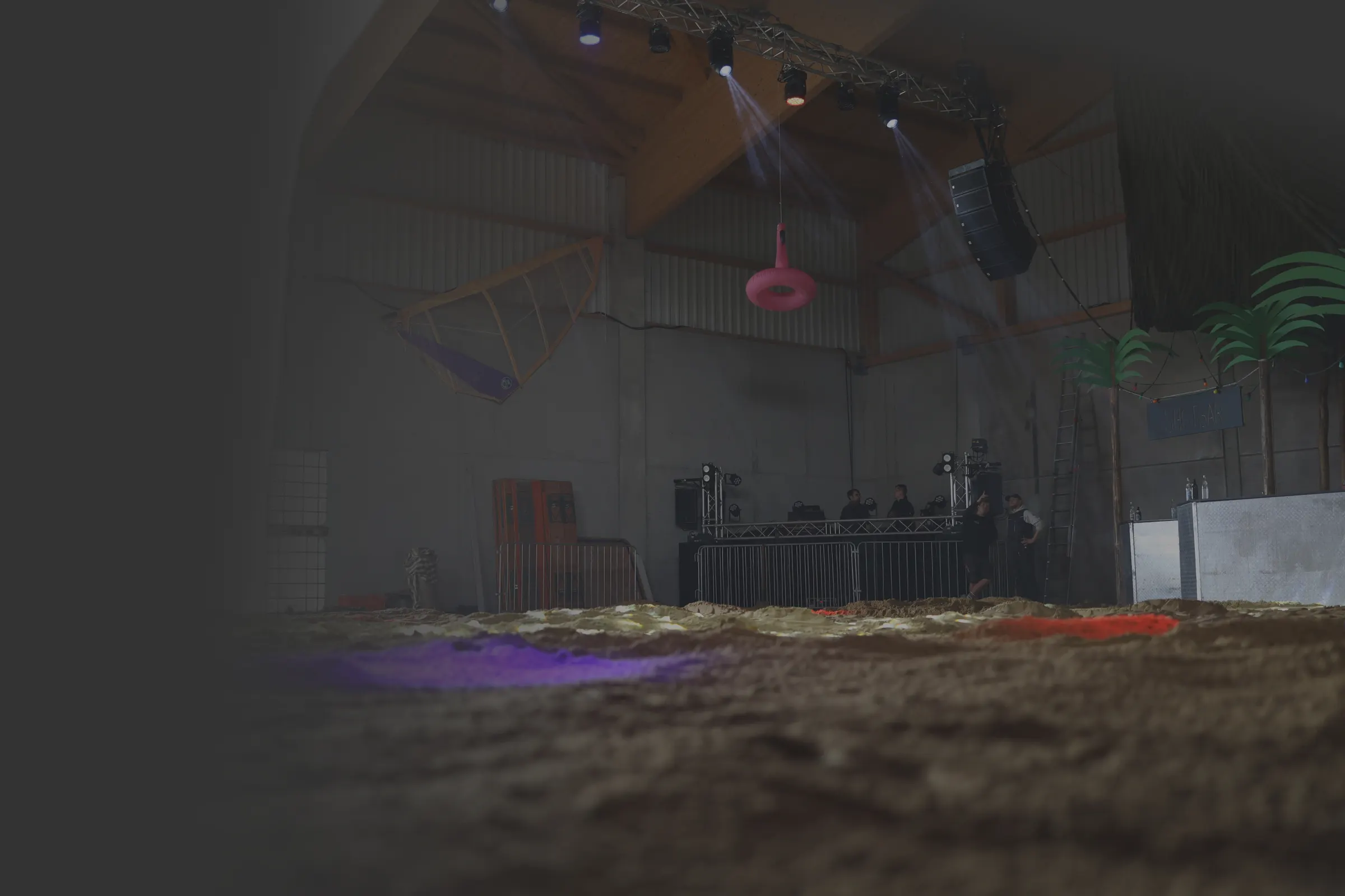 Hängende Lautsprecher und DJ-Pult in einer Eventhalle mit Sandboden