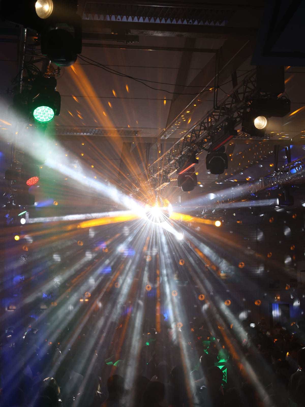 Discokugel mit weißen und orangen Lichtstrahlen über dem Publikum