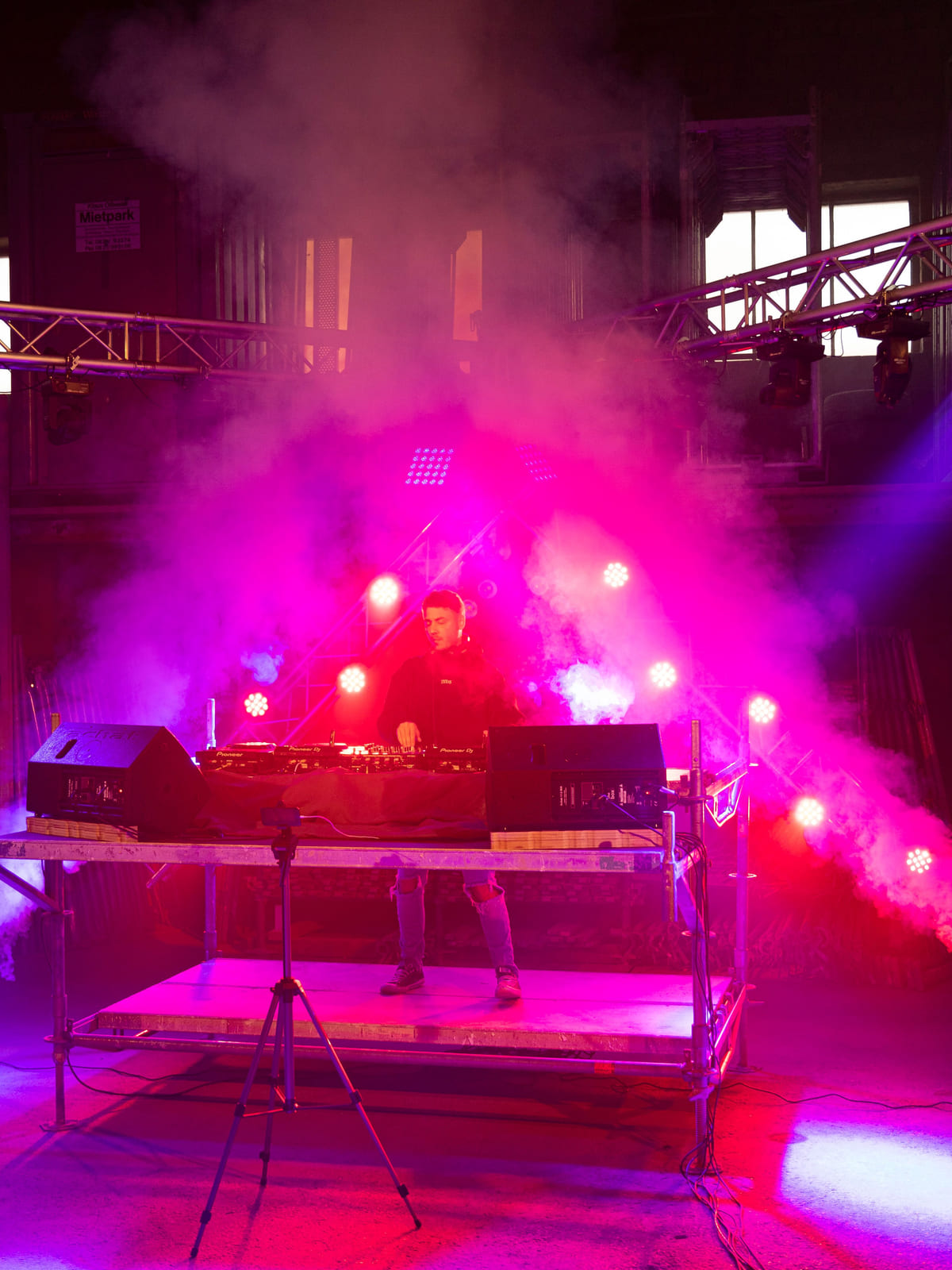 DJ auf einem Podest in magenta Nebel und lila Licht